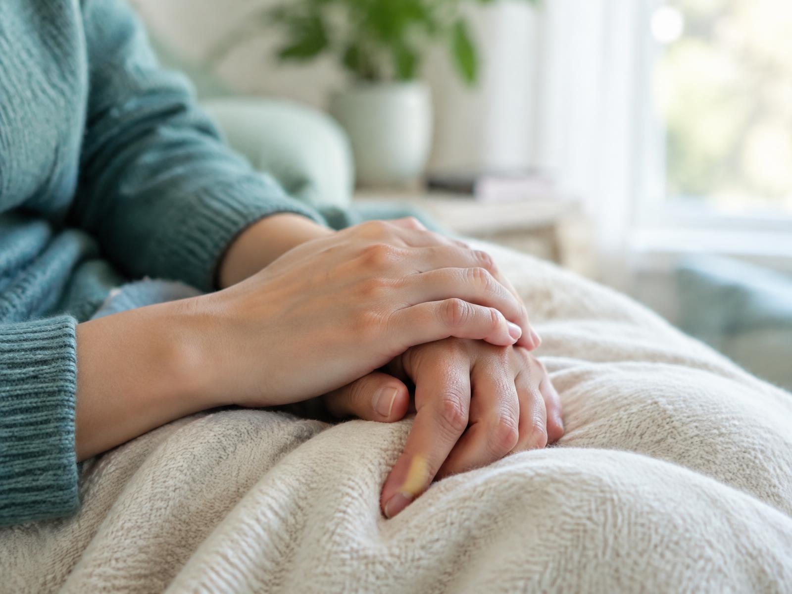Two hands resting gently on a cream blanket