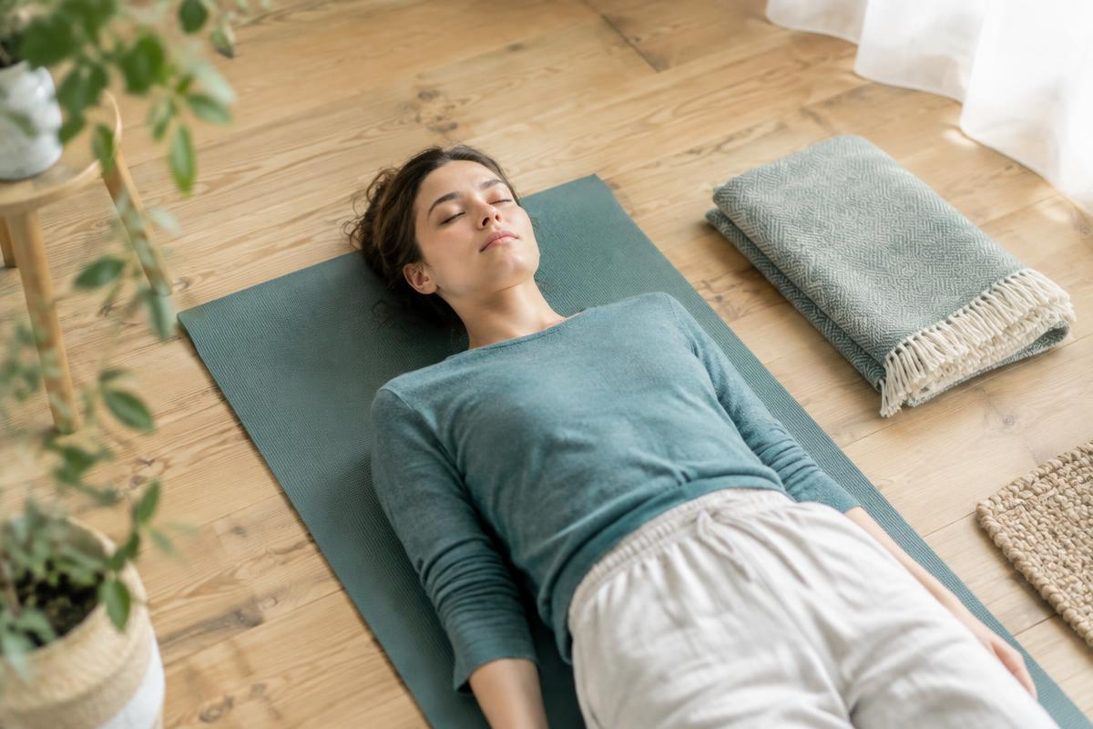 A person lying on a mat with their eyes closed, resting